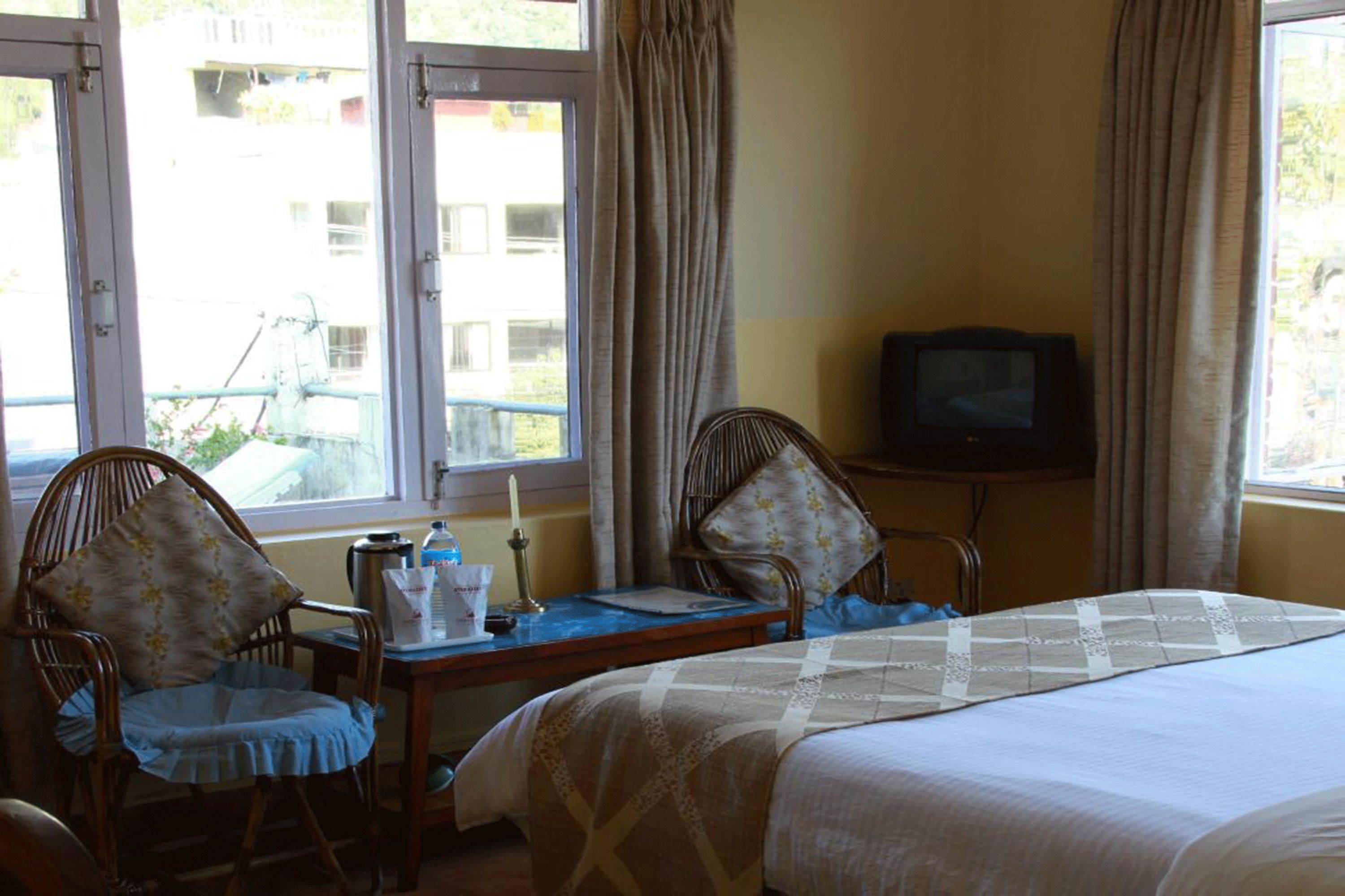 A hotel room with a bed, two chairs, a small table with a lamp, and a television.
