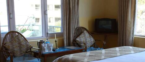 A hotel room with a bed, two chairs, a small table with a lamp, and a television.