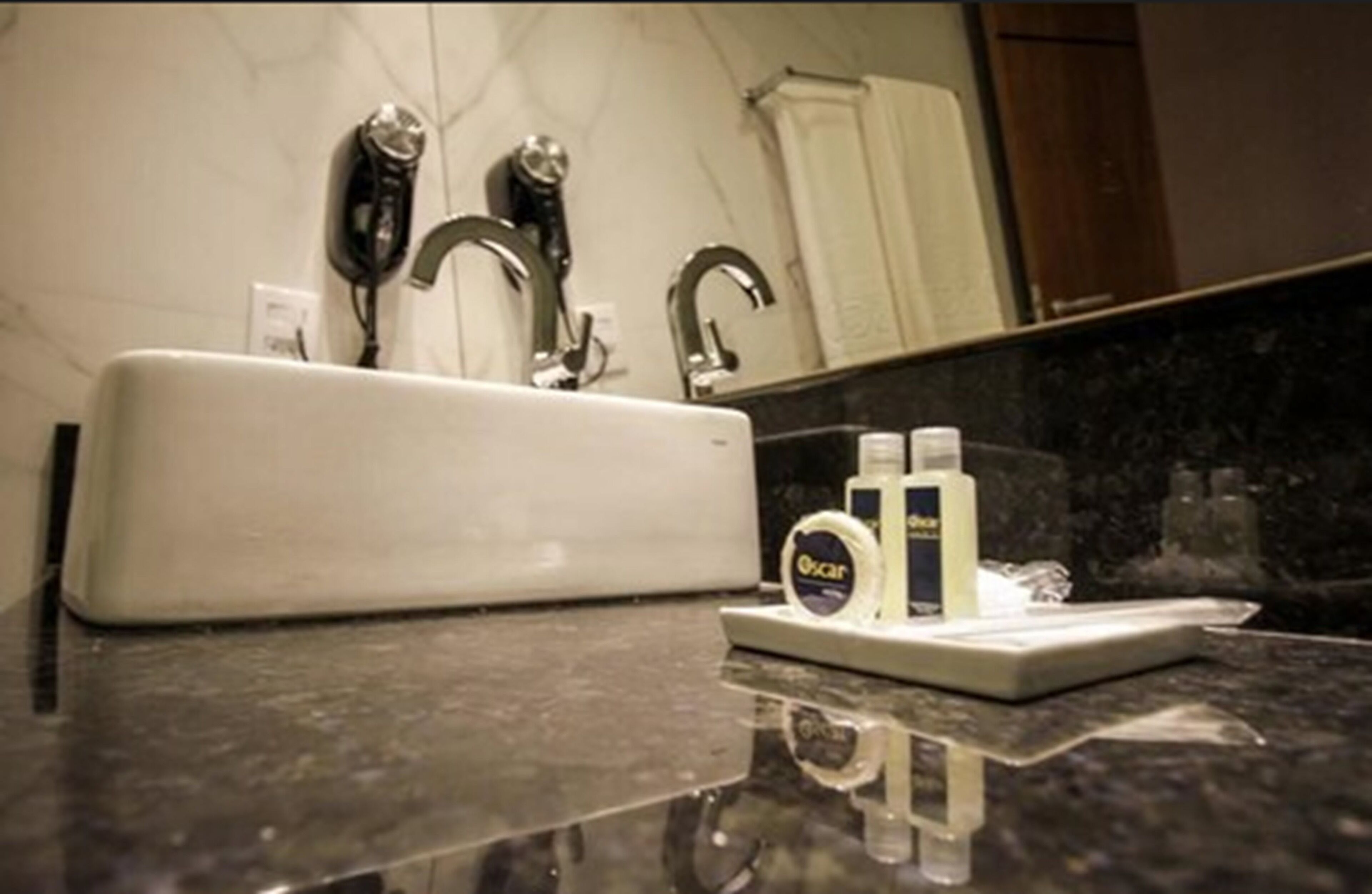 Un baño con un lavamanos blanco, dos grifos, un espejo y una encimera con dispensador de jabón y una botella.