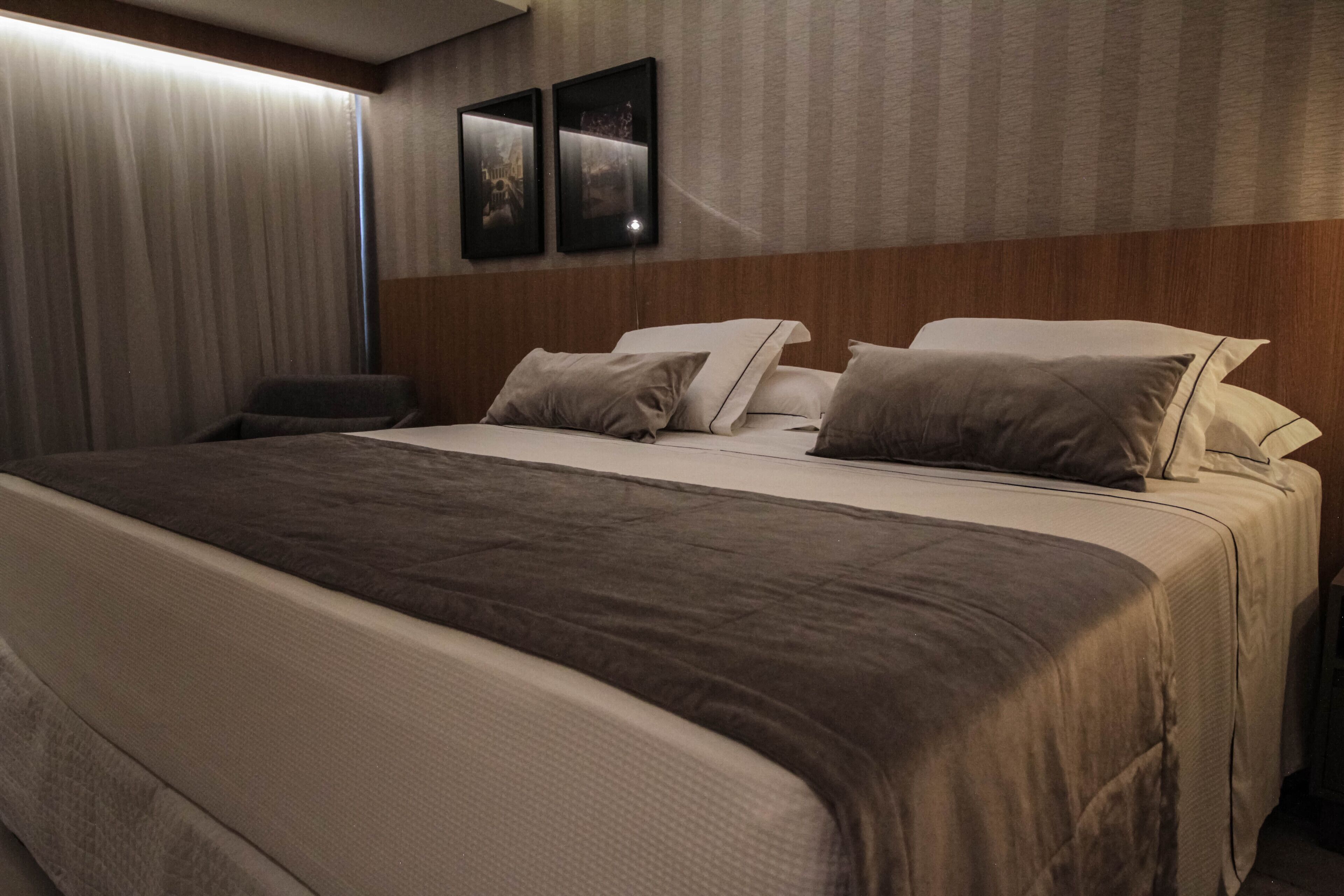 Habitación de hotel con una cama grande, cabecera, mesita de noche y dos cuadros enmarcados en la pared.