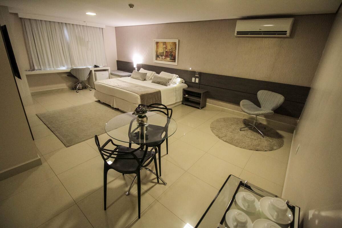 A hotel room with a bed, bedside table, chair, desk, and a small dining table with chairs.
