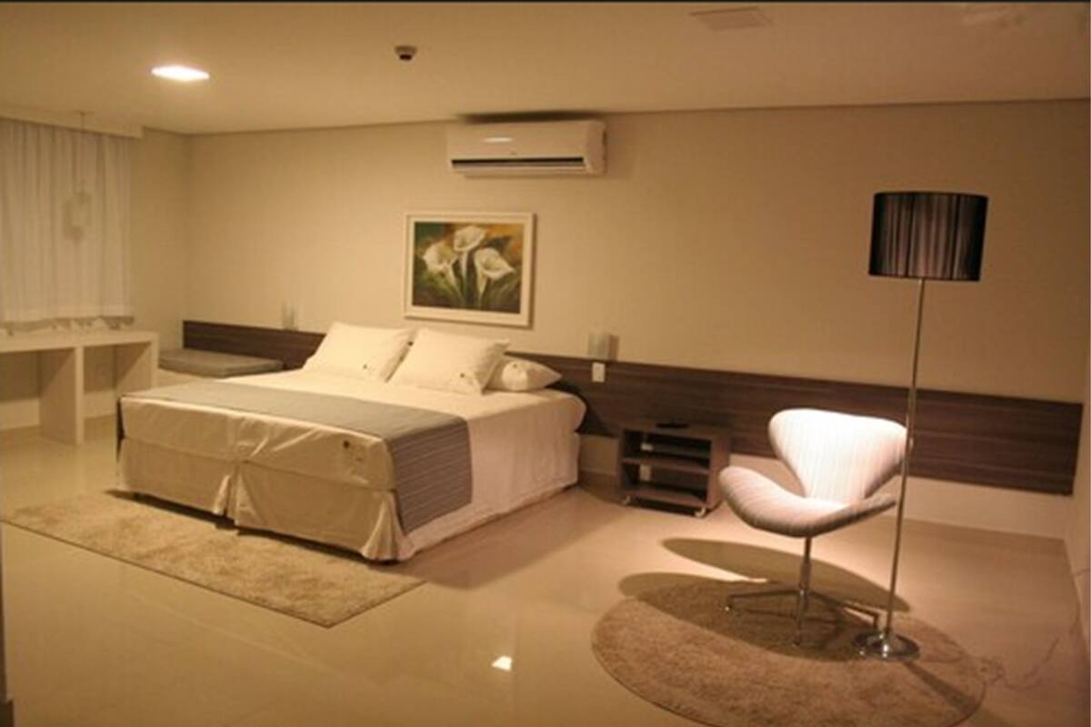 A modern bedroom with a bed, bedside table, lamp, and a painting on the wall.