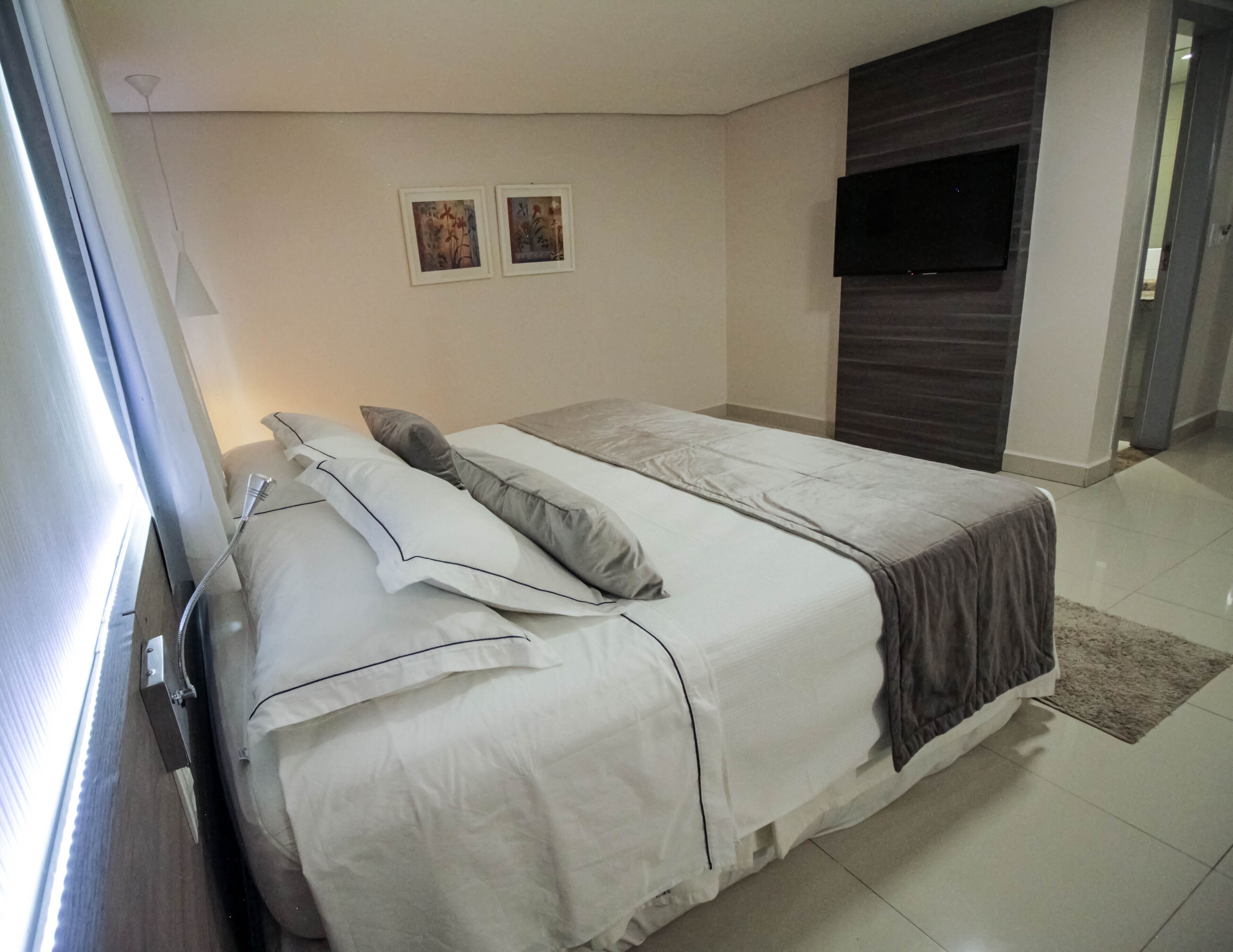 A neatly made bed with white linens and a gray blanket, a bedside table with a lamp, and two framed pictures on the wall.