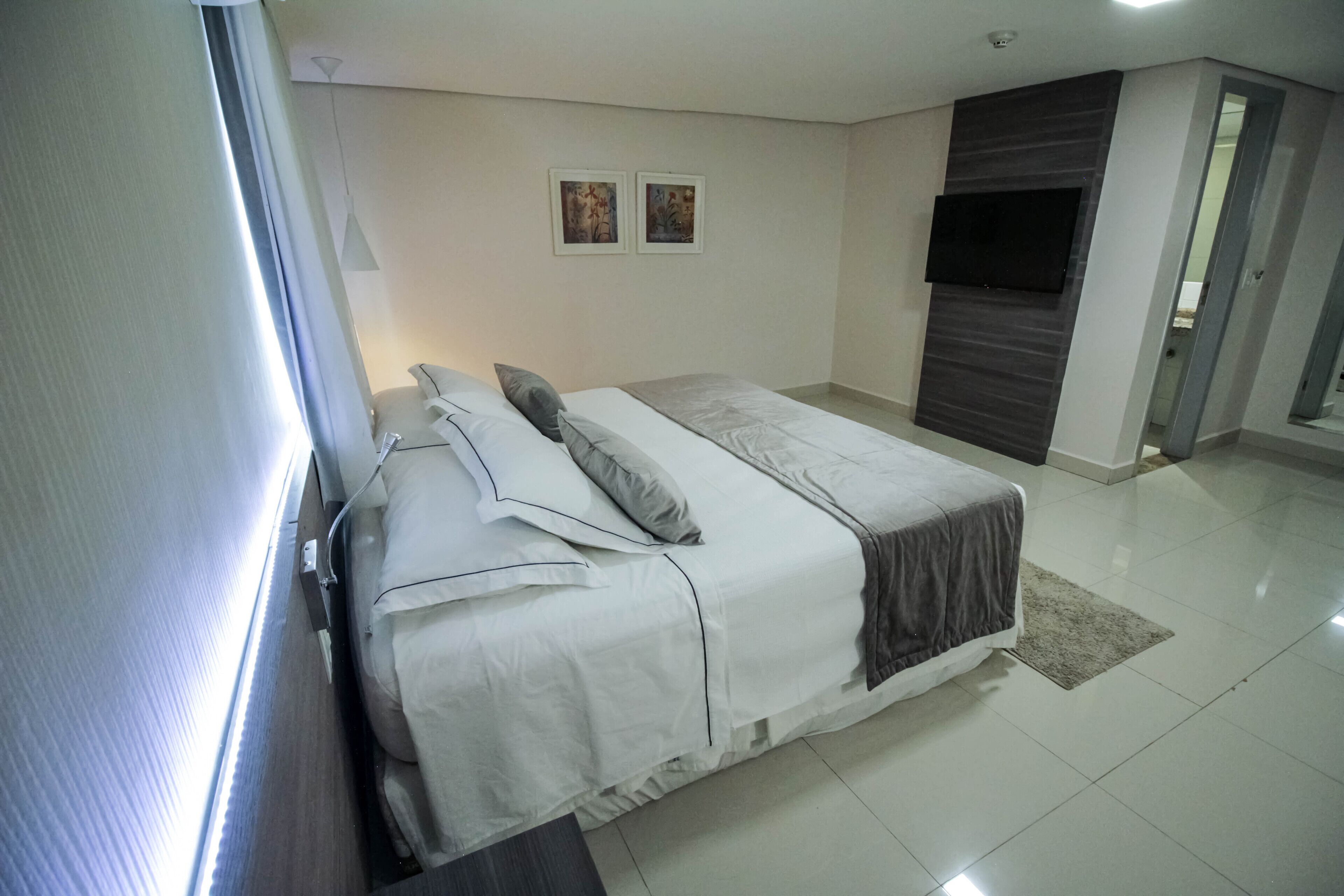 A modern bedroom with a bed, a flat-screen TV, and two framed pictures on the wall.