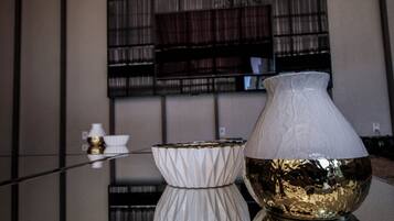 Un interior moderno con una mesa de vidrio reflectante que muestra un jarrón blanco y un cuenco dorado.