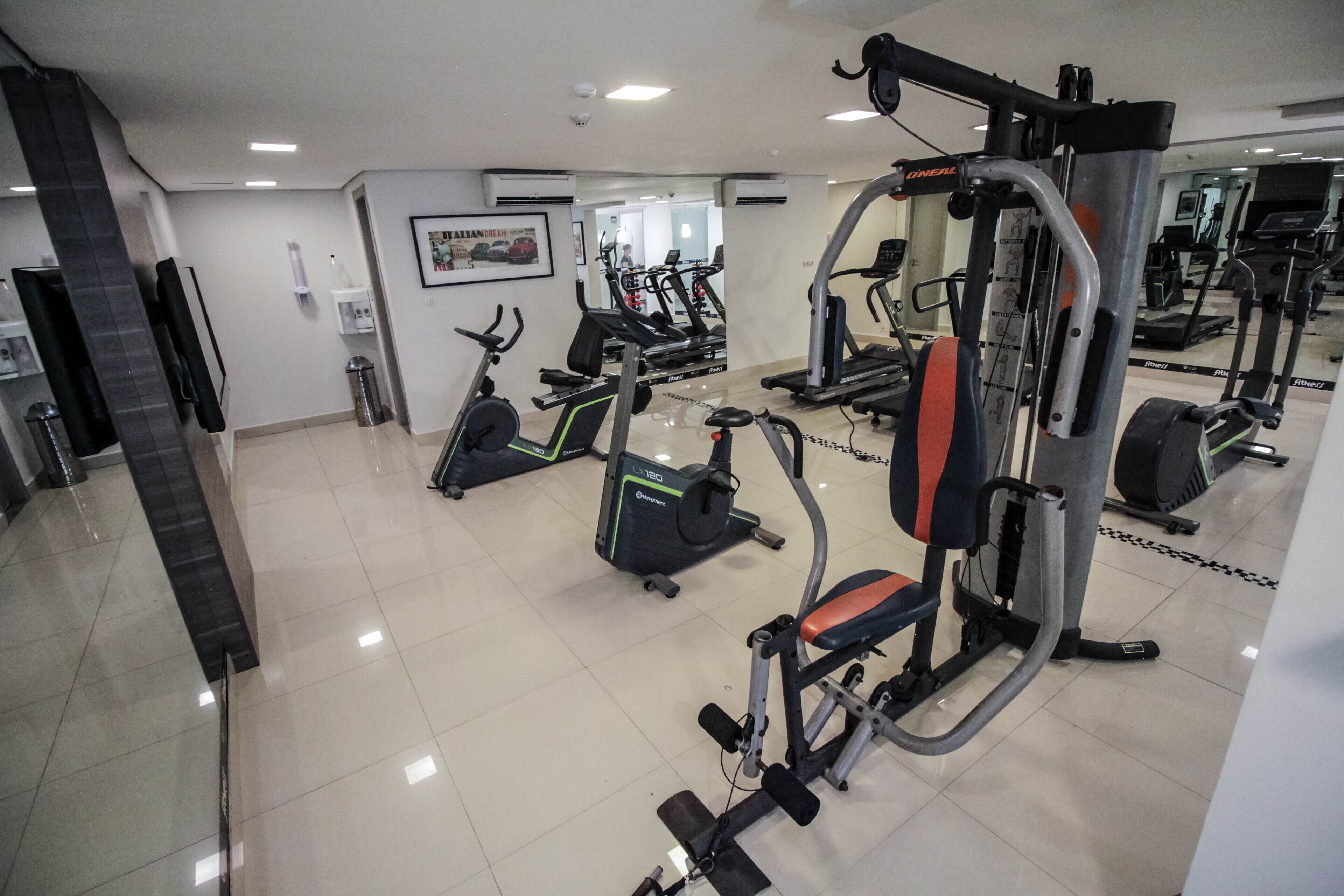 A gym with various exercise machines, a mirror, and a clean, tiled floor.