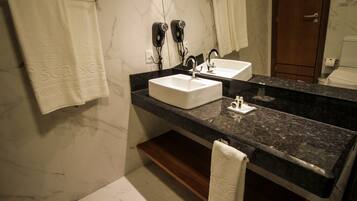 Un baño con pared de mármol, encimera negra, dos lavamanos y un perchero para toallas.