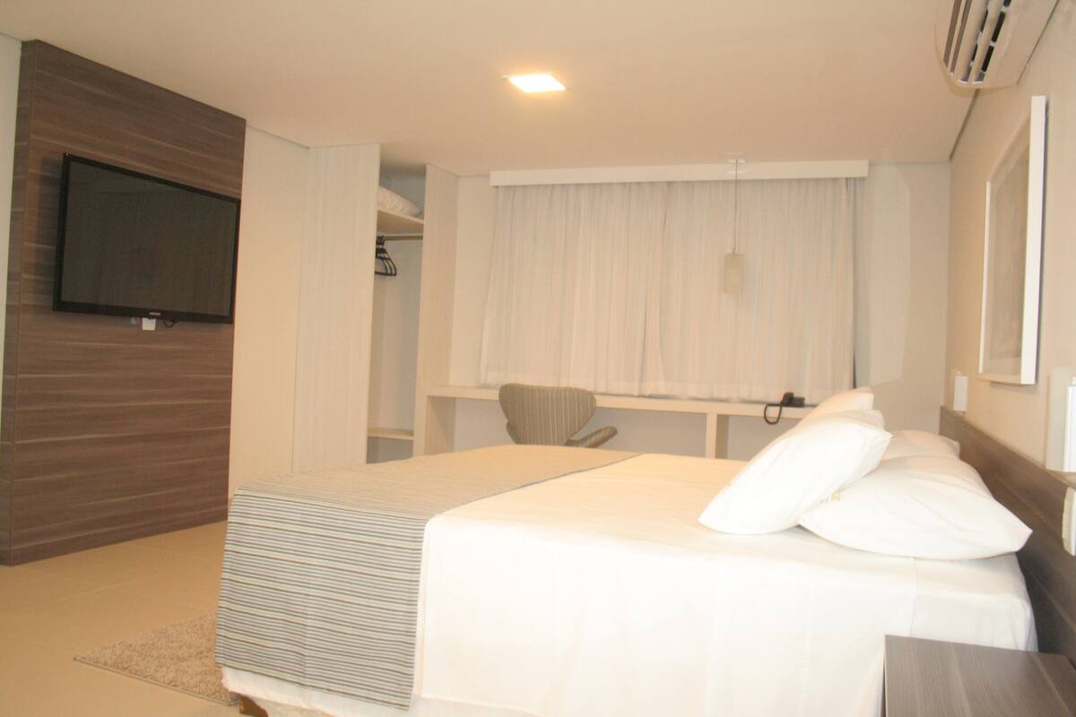 A hotel room with a bed, a TV mounted on the wall, a desk, and a chair.
