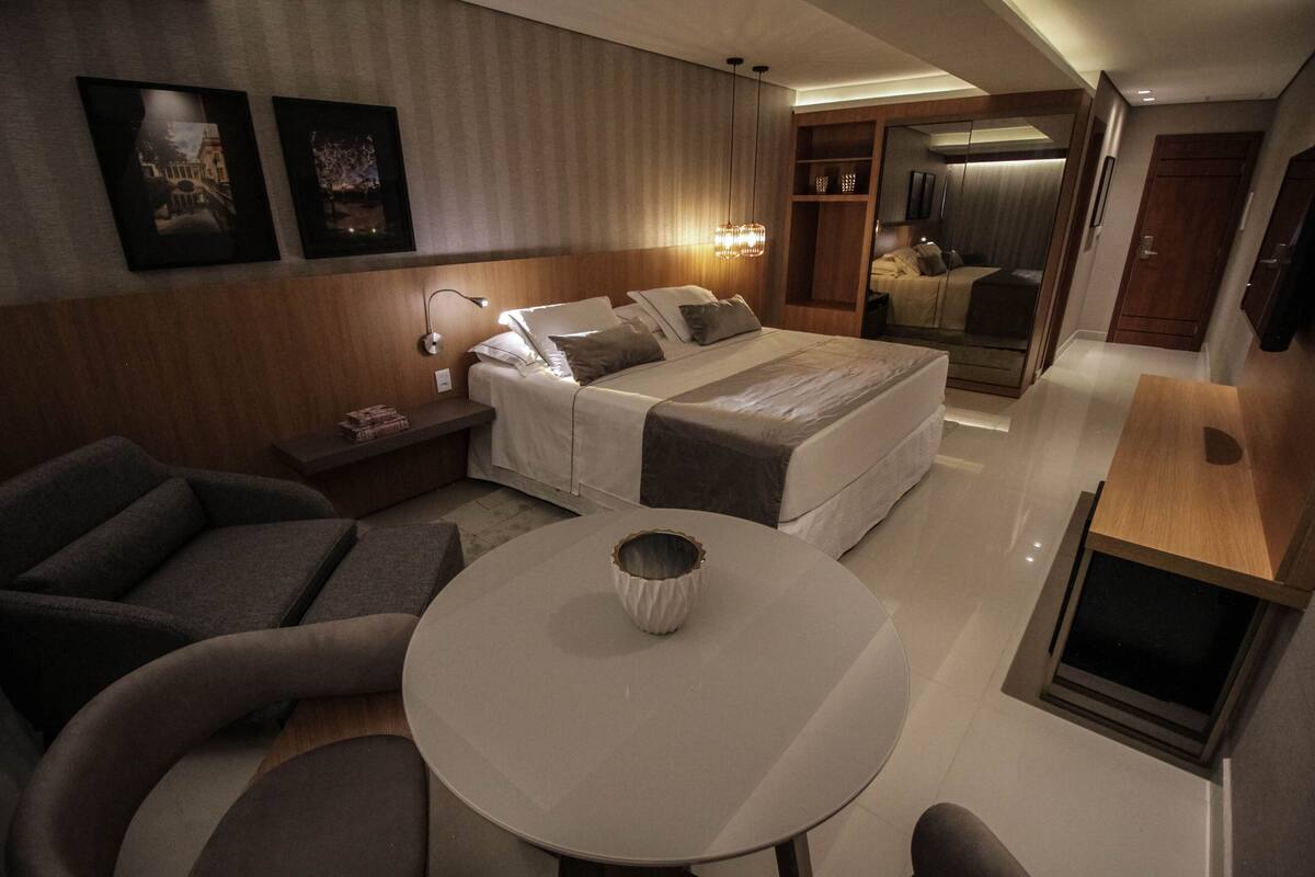 A modern hotel room with a bed, a round table, a sofa, and a mirror.