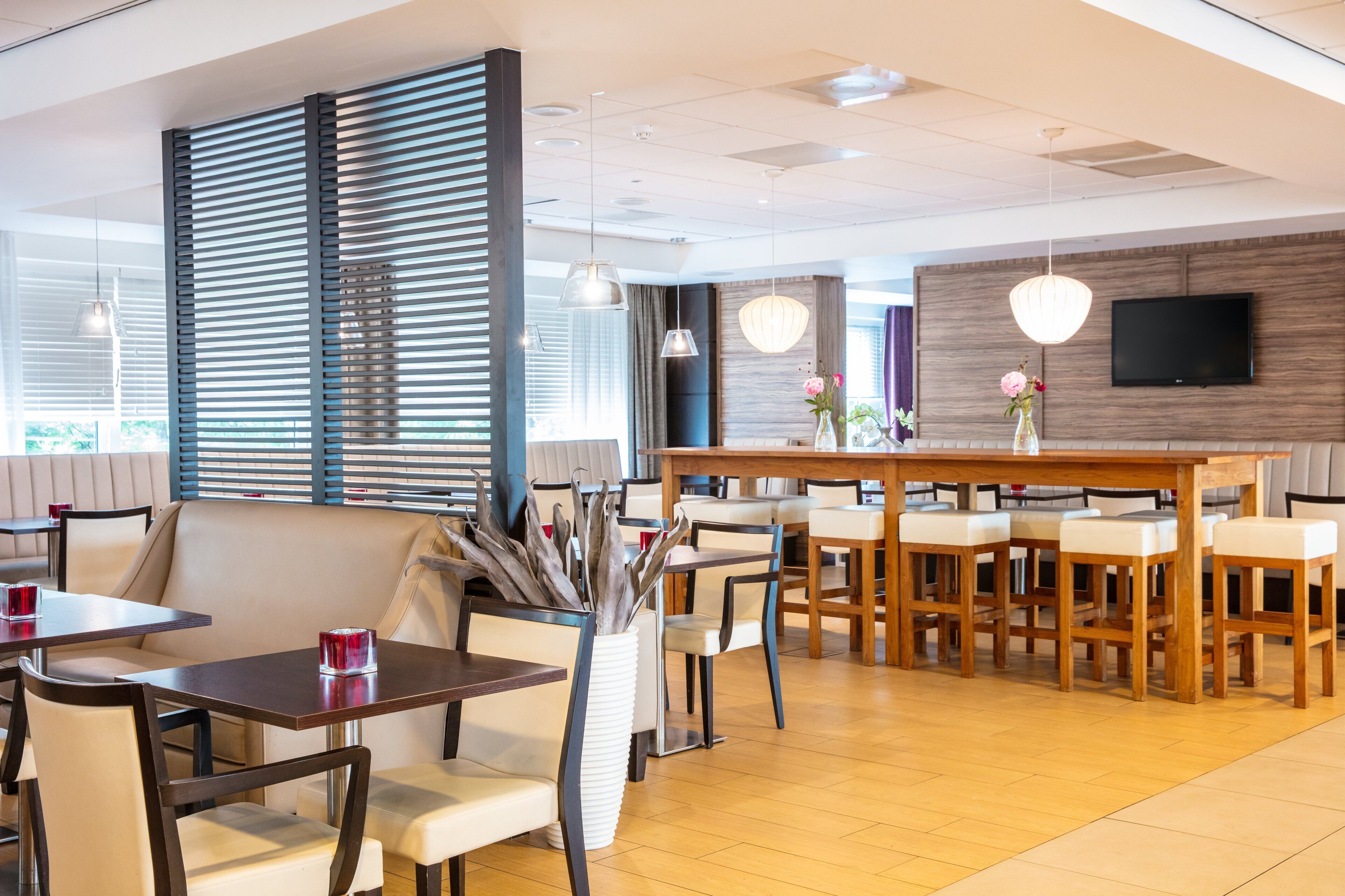 A modern dining area with a wooden bar, cushioned seating, and pendant lighting.