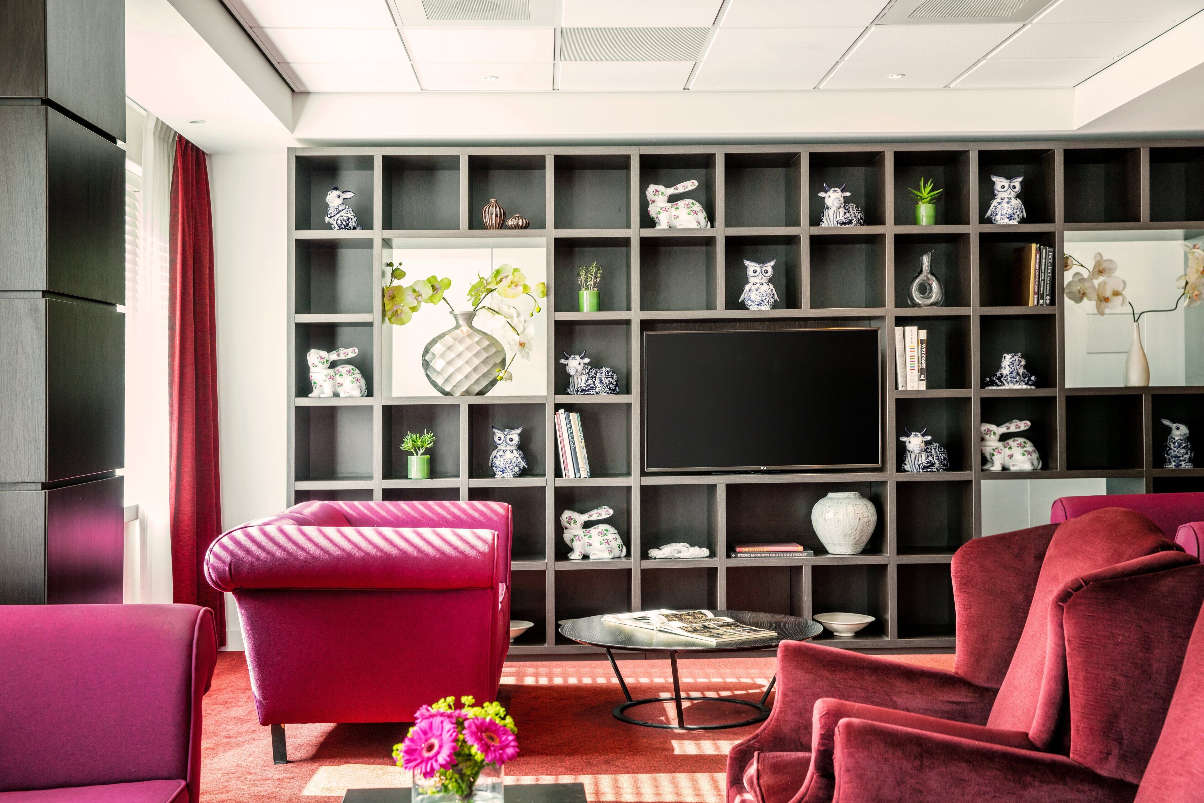 Un salon moderne doté d’un grand téléviseur à écran plat, de fauteuils à revêtement rouge et d’une bibliothèque remplie d’objets décoratifs.