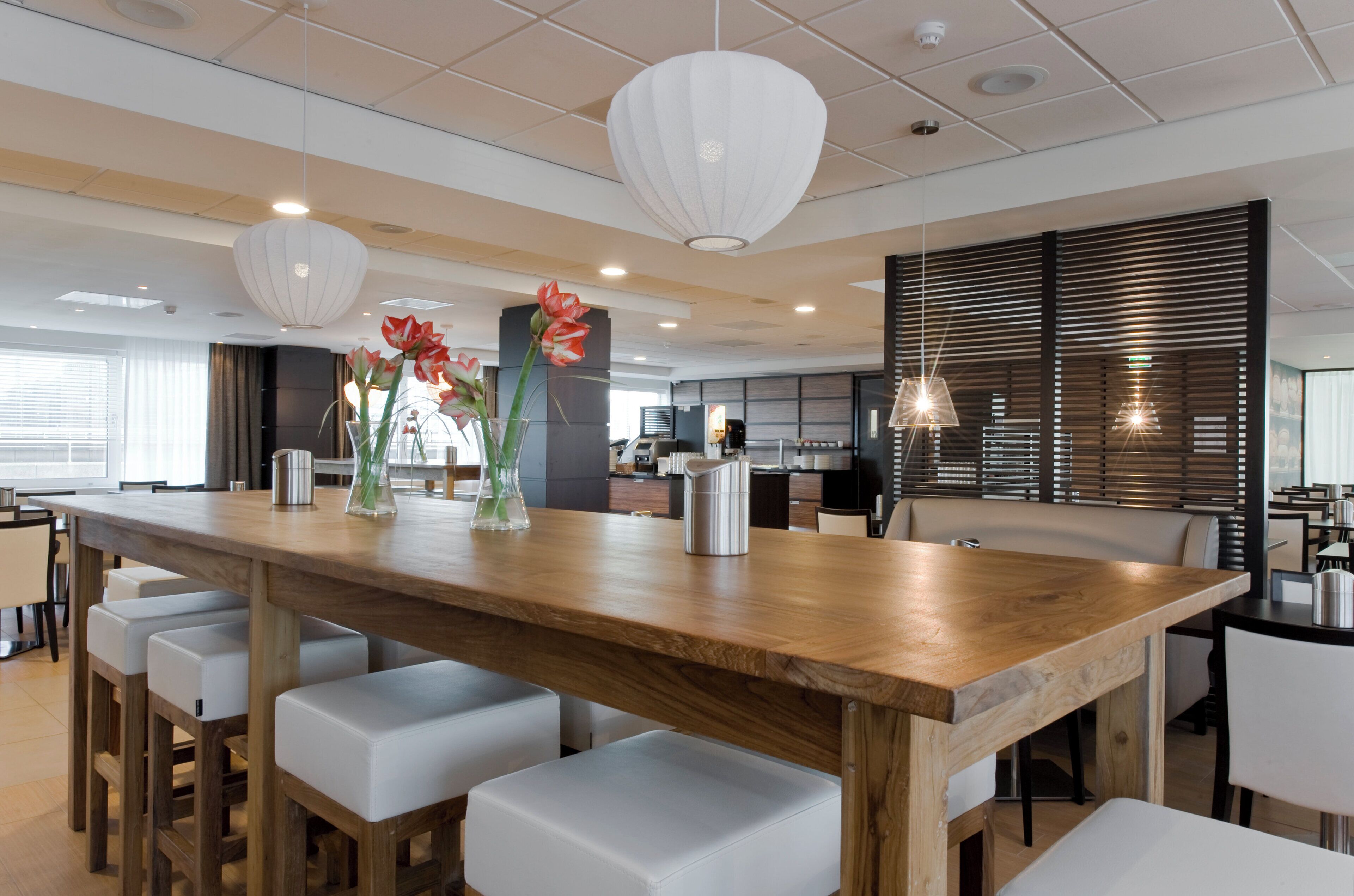 A modern dining area with a wooden table, white cushioned chairs, and decorative vases with flowers.