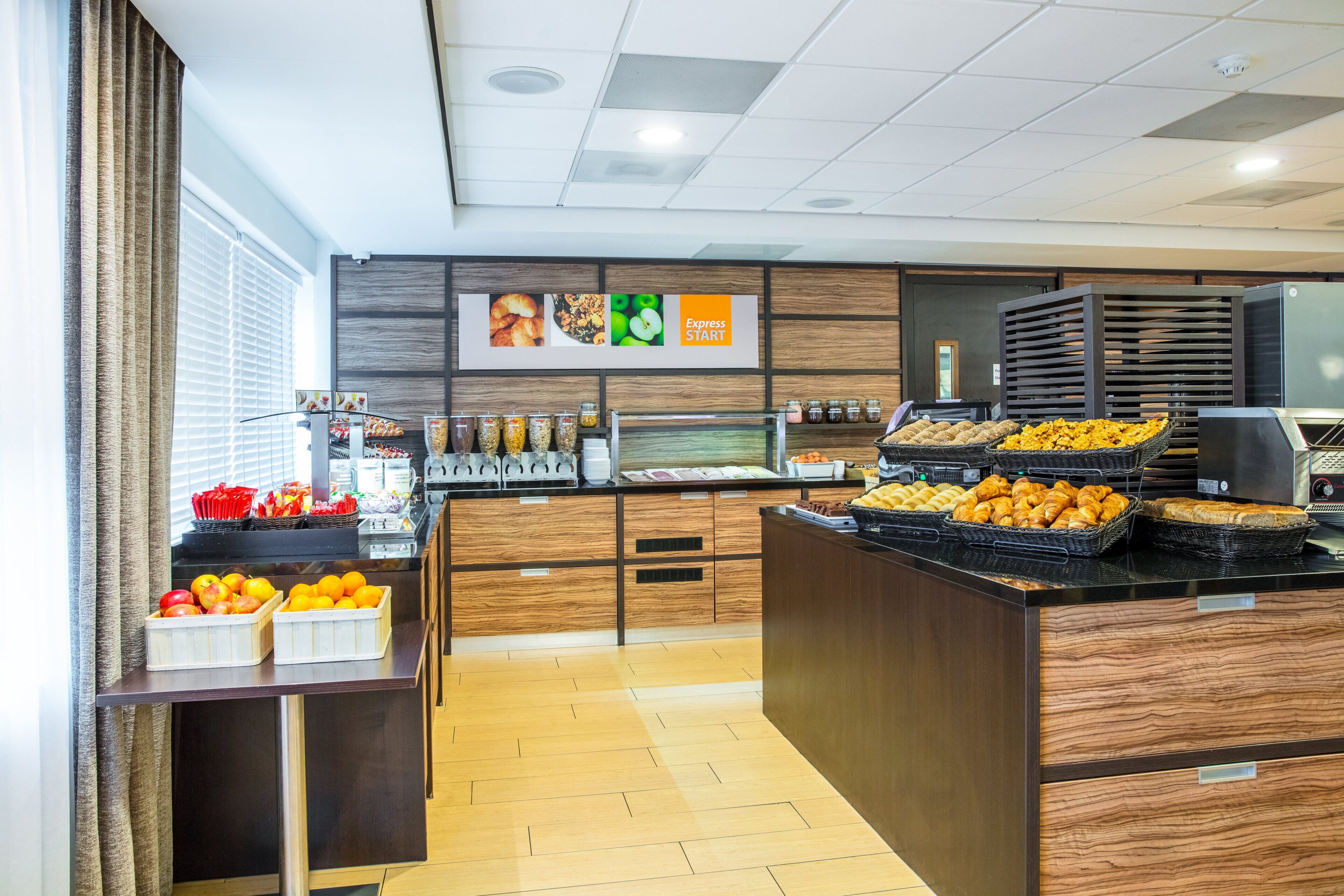 Ein Frühstücksbereich mit verschiedenen Speisen, einer Kaffeemaschine und einem Schild, das den Beginn des Buffets kennzeichnet.