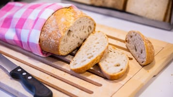 A loaf of bread wrapped in a pink and white checkered cloth on a wooden cutting board.