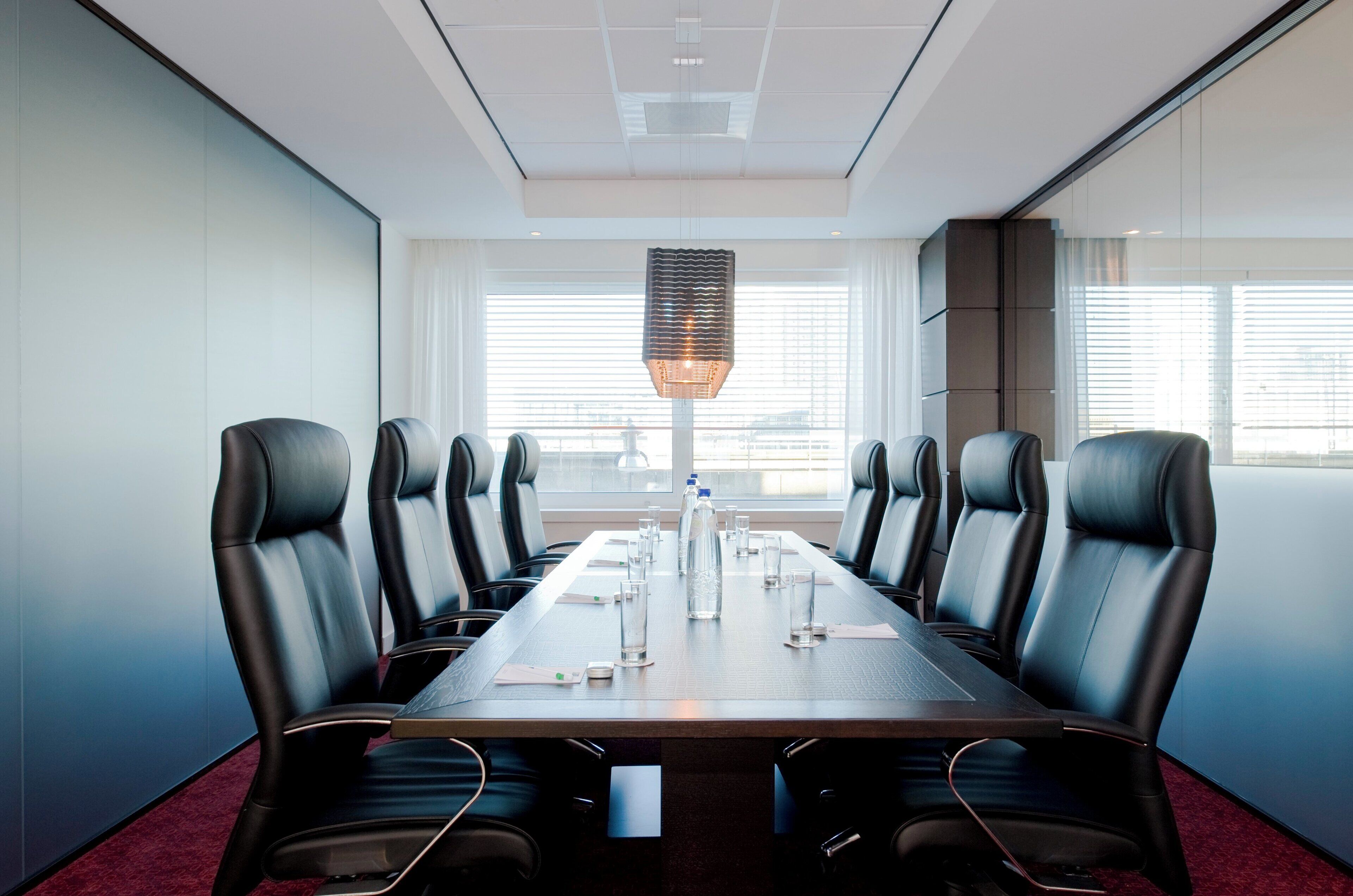 A conference room with a long table, black leather chairs, and a city view through large windows.