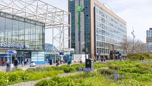 A modern hotel with a prominent 'Holiday Inn Express' sign, a glass facade, and a surrounding landscaped garden. - Holiday Inn Express Amsterdam - Sloterdijk Station by IHG (Amsterdam)