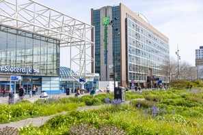 Een modern hotel met een opvallend 'Holiday Inn Express' bord, een glazen gevel en een aangelegde tuin eromheen.