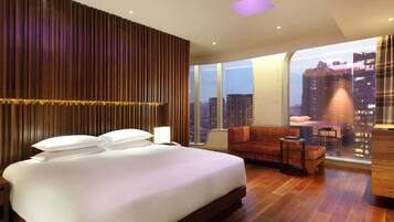 Una habitación de hotel moderna con una cama grande, un sofá, una mesita y vistas a la ciudad.