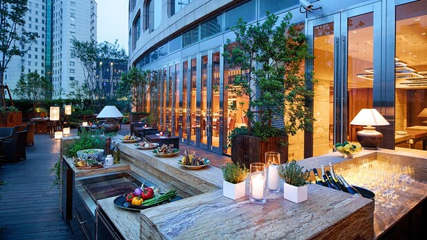 Een dakterras met terrasplekken, een bar met flessen en glazen, en uitzicht op een modern gebouw.