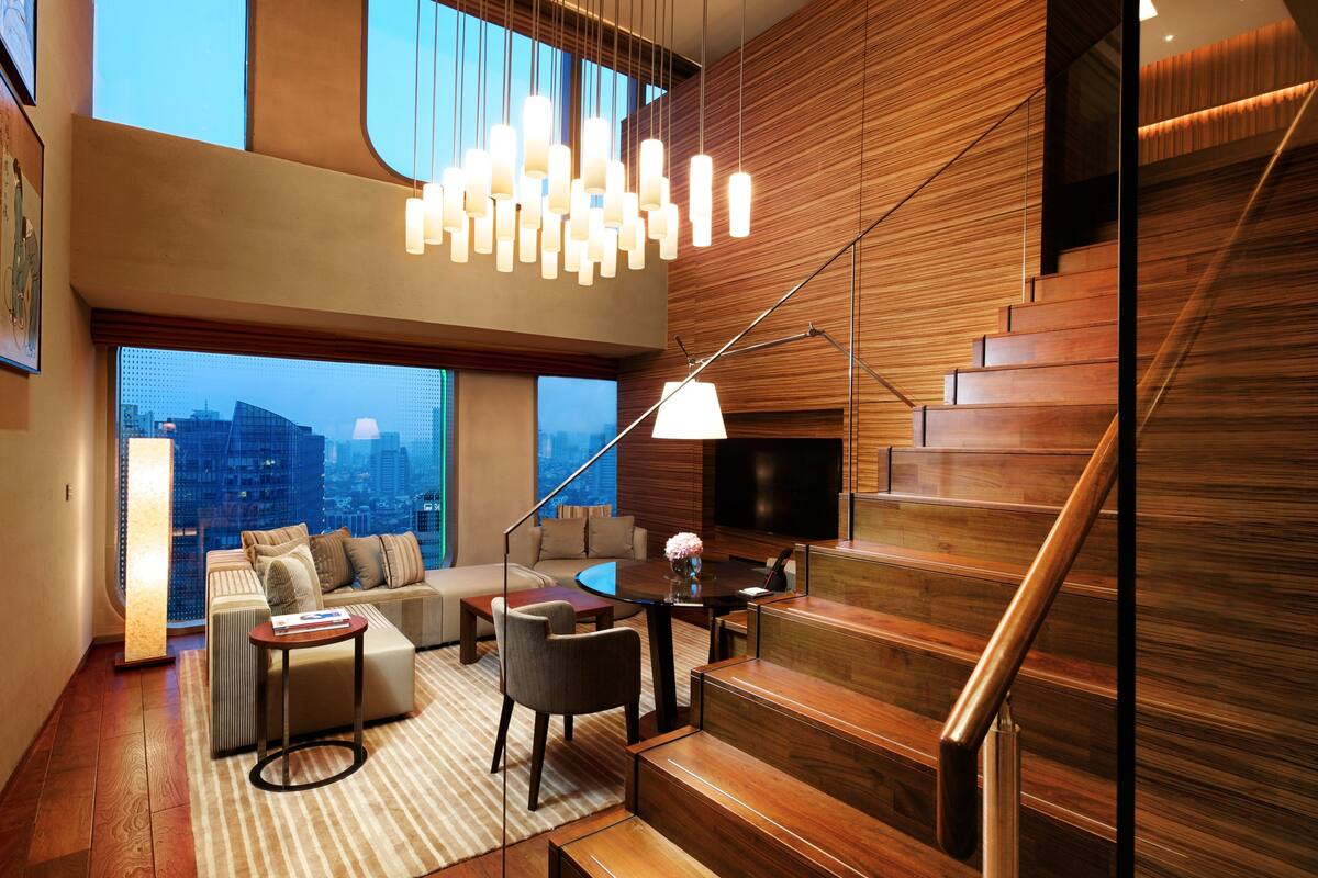 Uma sala de estar moderna com escada, uma janela ampla com vista para a cidade e um candelabro.