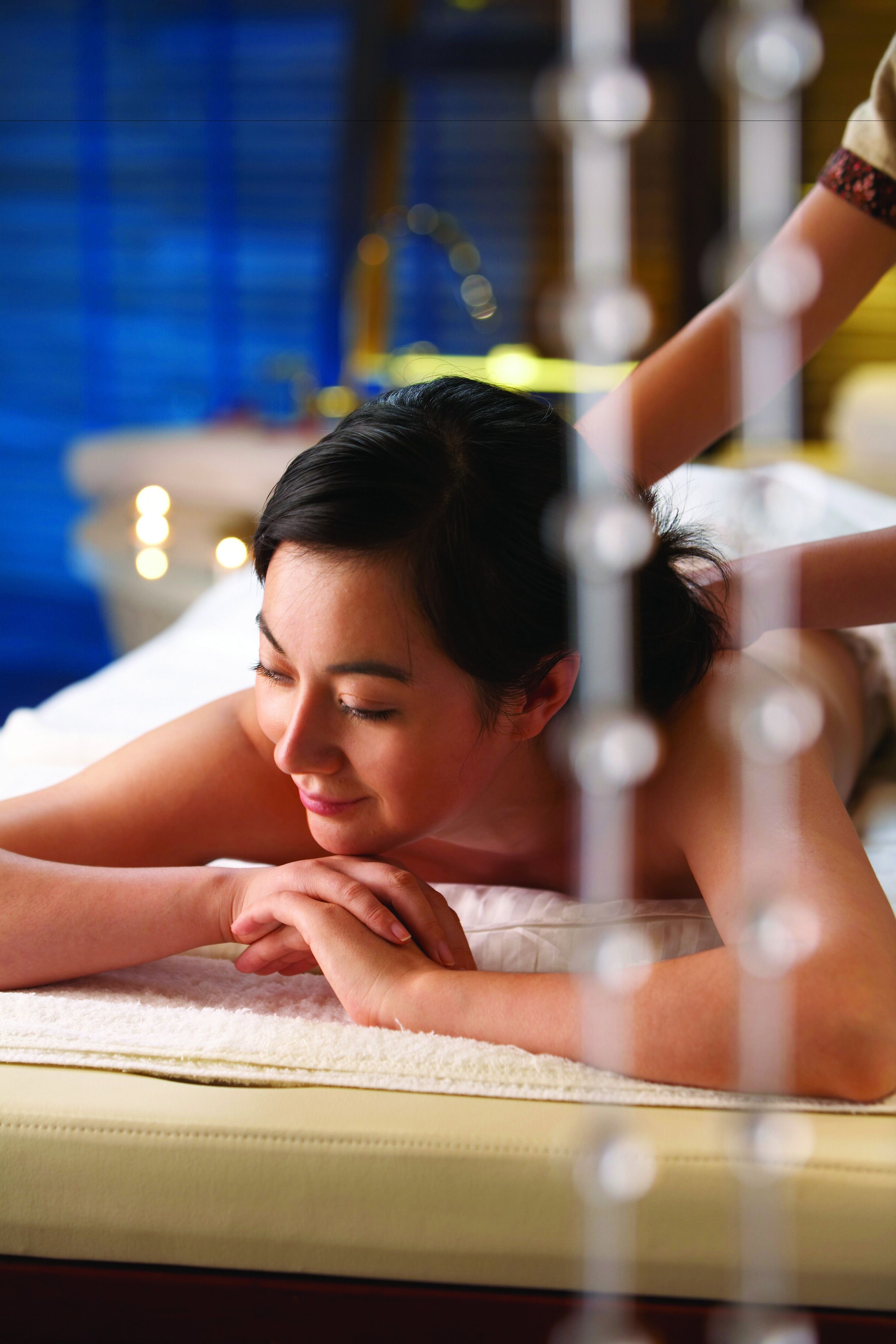 A person lying on a massage table in a room with a blue wall and a bed in the background.