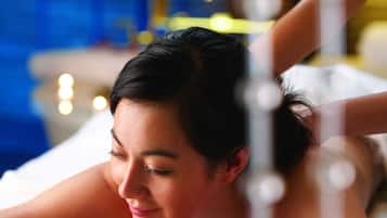 A person lying on a massage table in a room with a blue wall and a bed in the background.