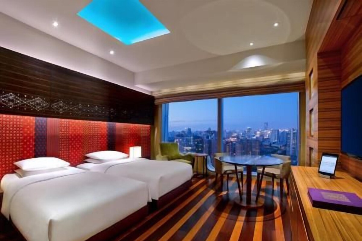 A hotel room with a city view, two beds, a desk, and a round table.