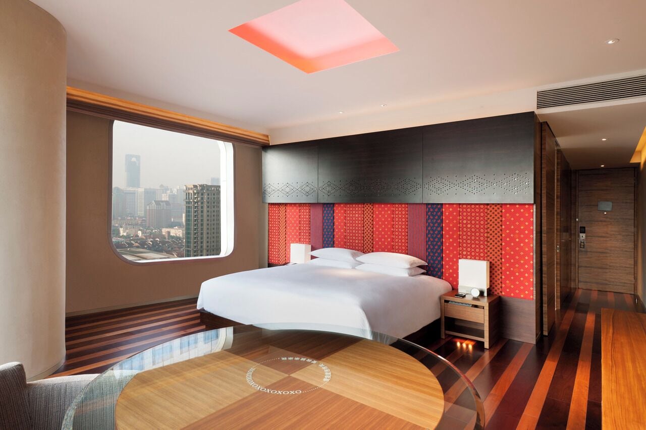 Habitación de hotel moderna con una cama grande, vistas a la ciudad, una mesa de comedor redonda y un diseño de techo original.