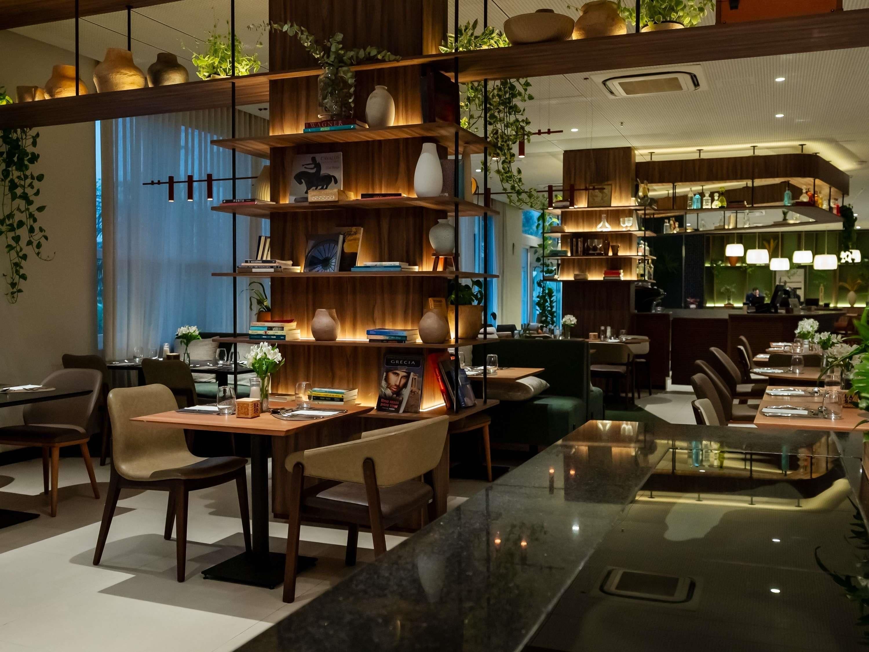 Un interior de restaurante moderno con estantes de madera, mesas, sillas e iluminación ambiental.