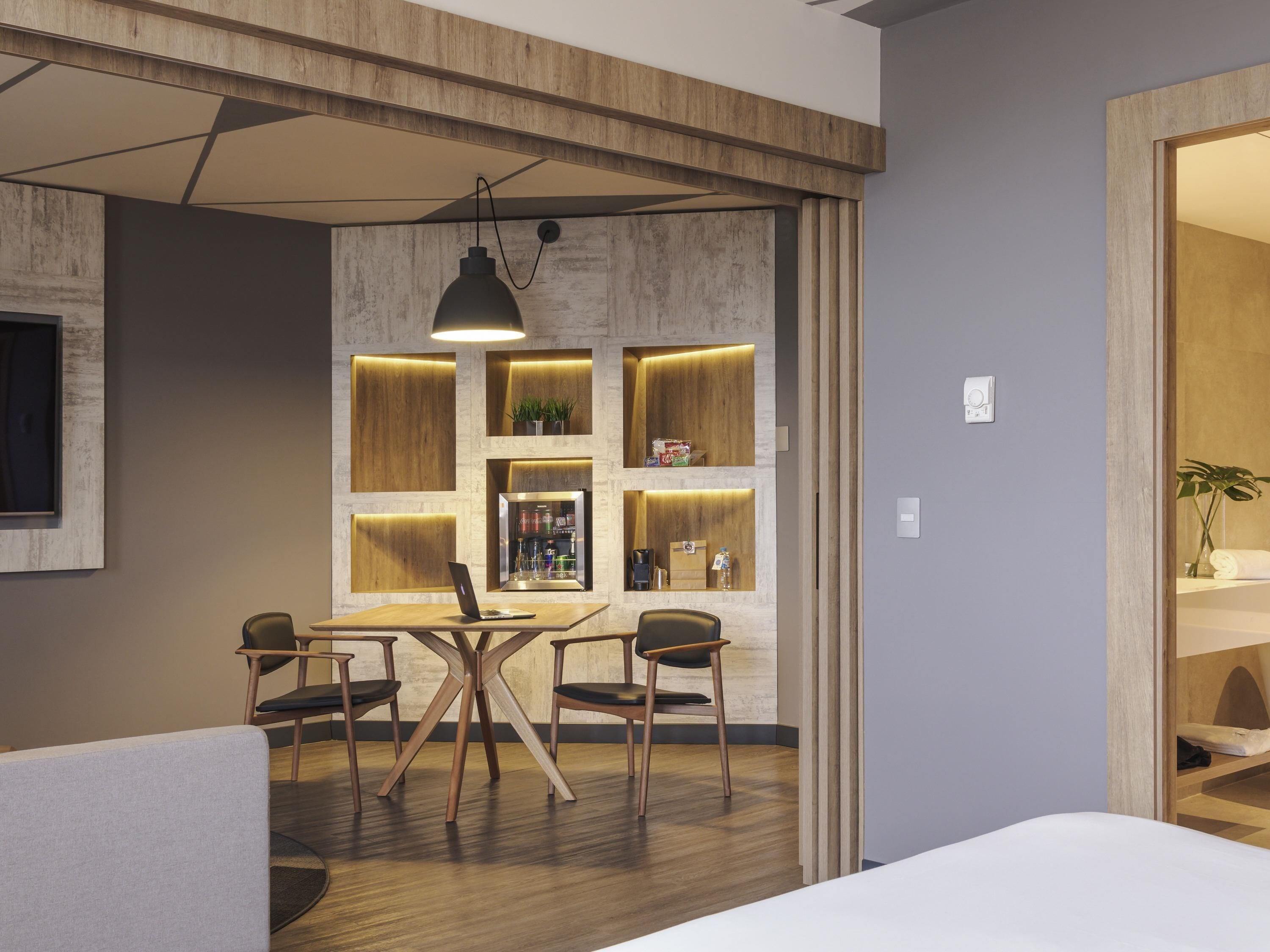 A modern room with a wooden dining table, four chairs, a hanging light fixture, and built-in shelving with various items.