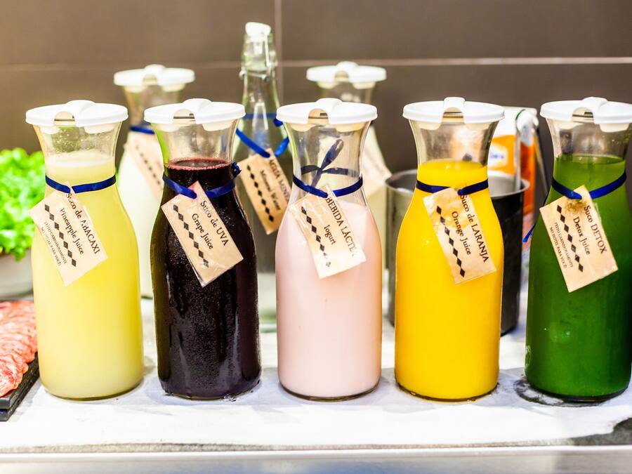 A variety of colorful beverages in glass bottles with labels, displayed on a counter.