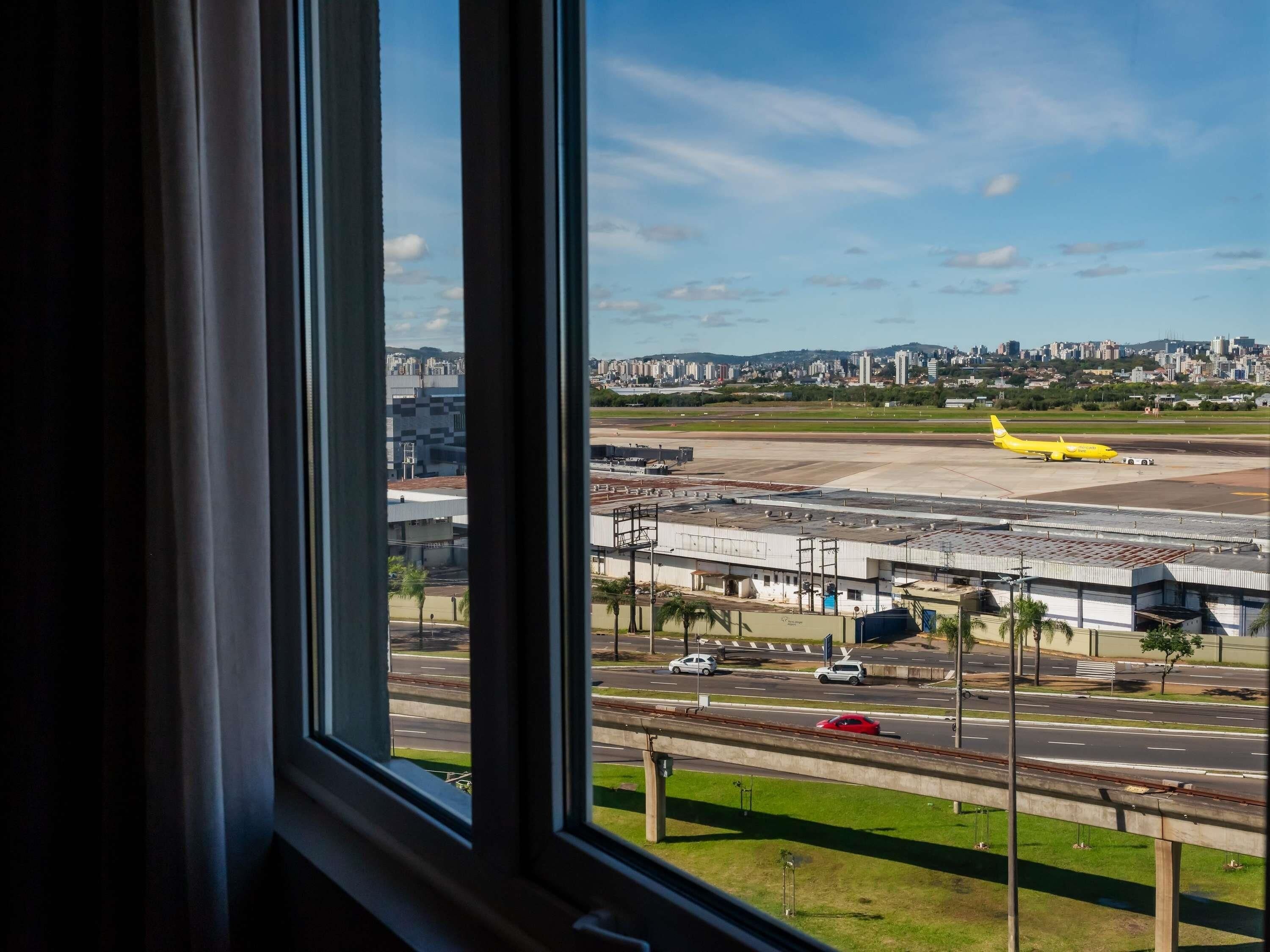 Blick auf ein Flughafen-Gelände mit einem gelben Flugzeug auf der Startbahn, Gebäuden im Hintergrund und einer Straße mit Fahrzeugen.