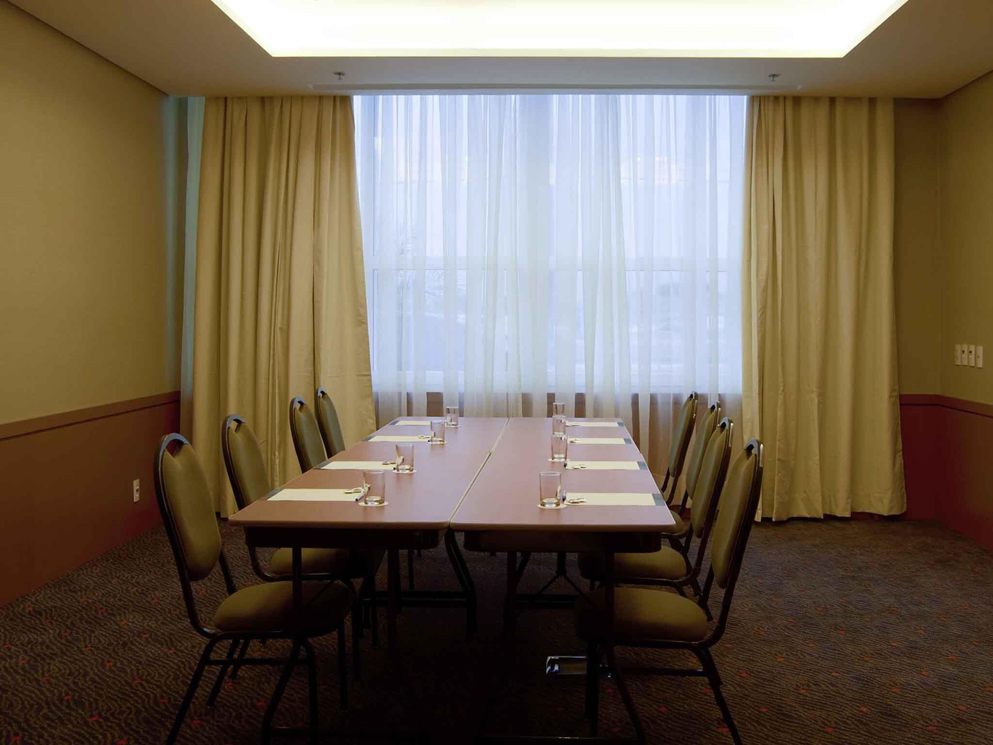 Uma sala de conferências com uma mesa comprida, cadeiras e uma janela grande com cortinas.