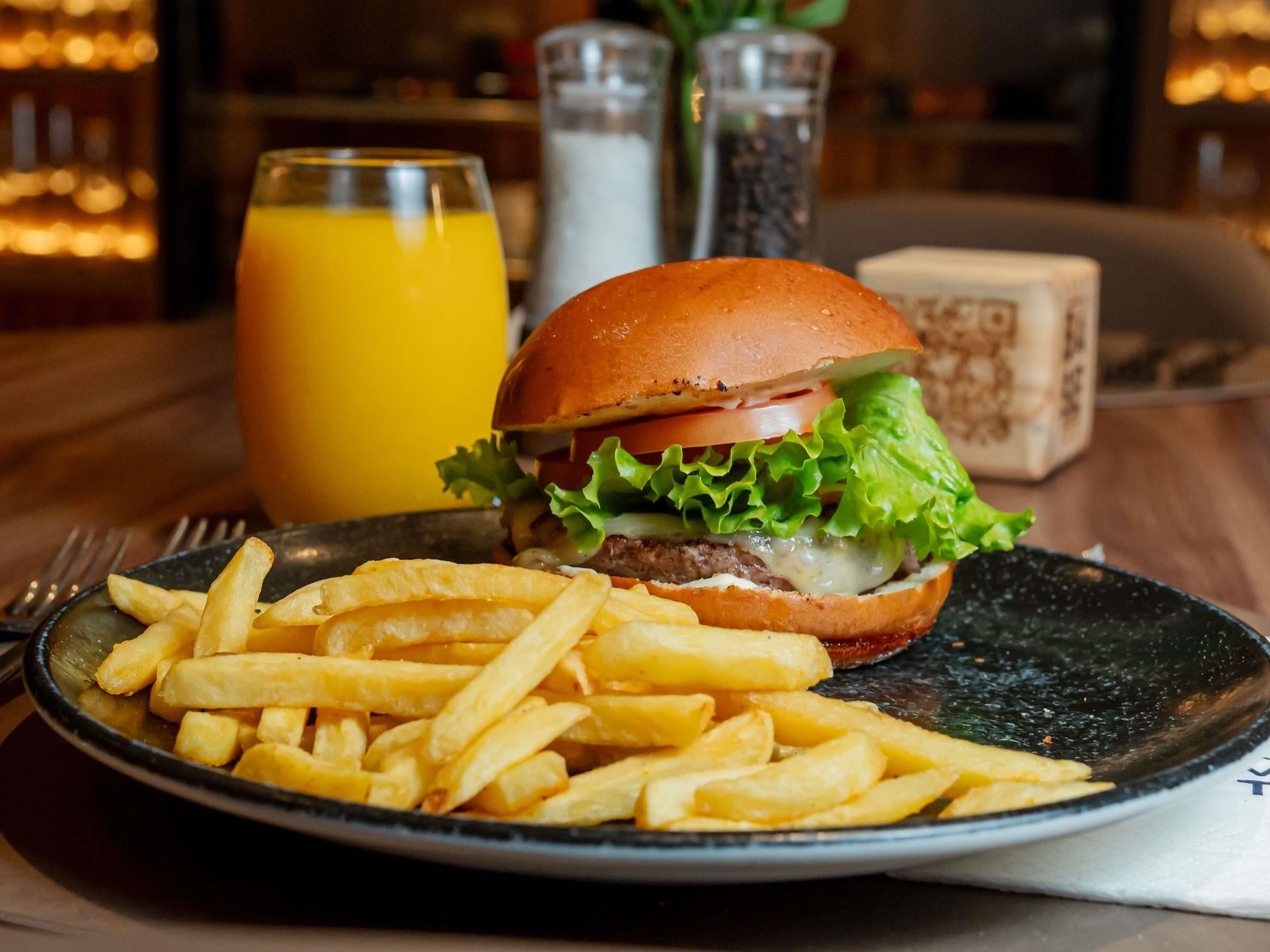Un repas composé d’un hamburger, de frites et d’un verre de jus d’orange, le tout posé sur une table.
