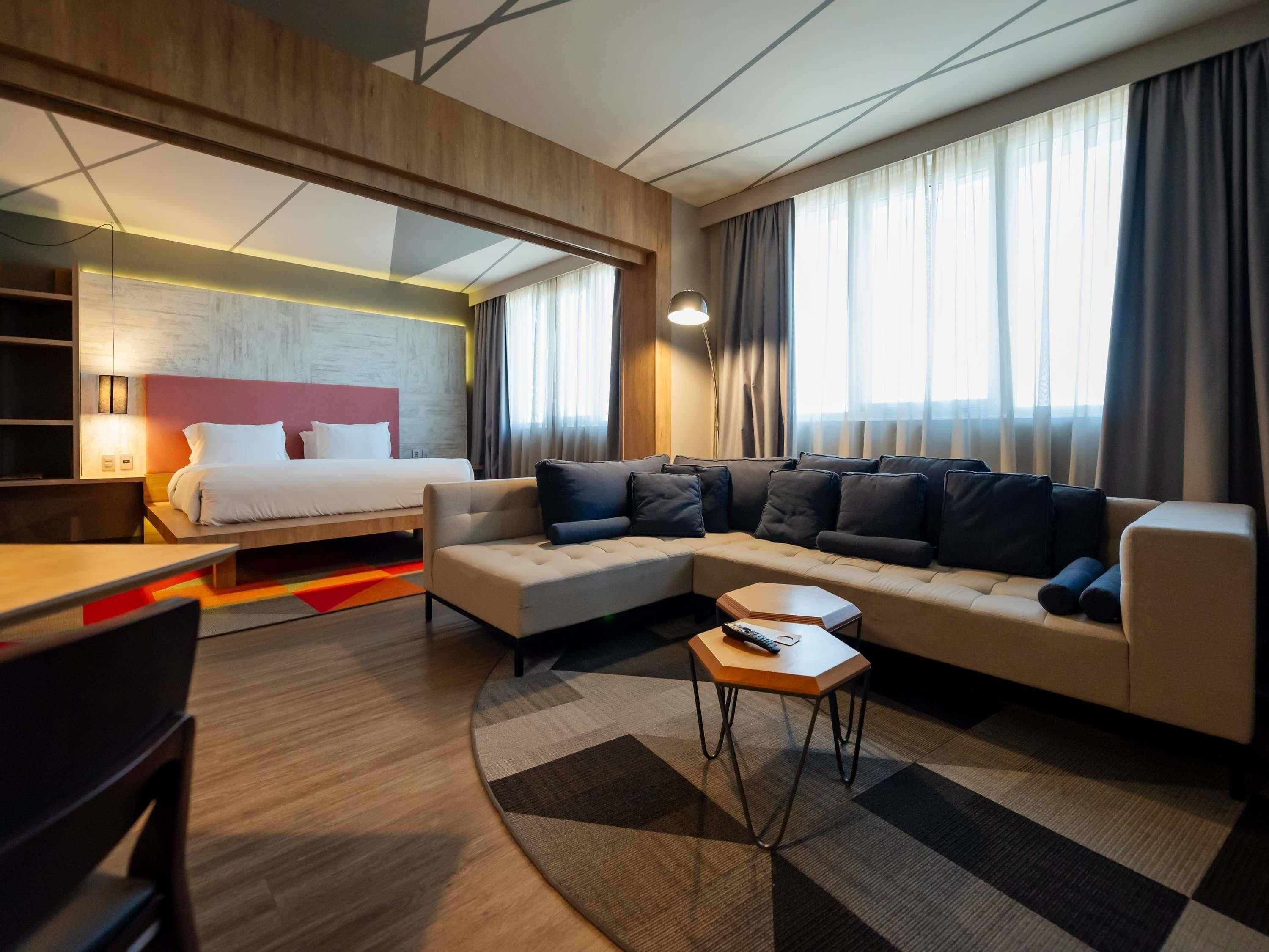Ein modernes Hotelzimmer mit einem Bett, einer Couch und einem kleinen Tisch mit einer Fernbedienung.
