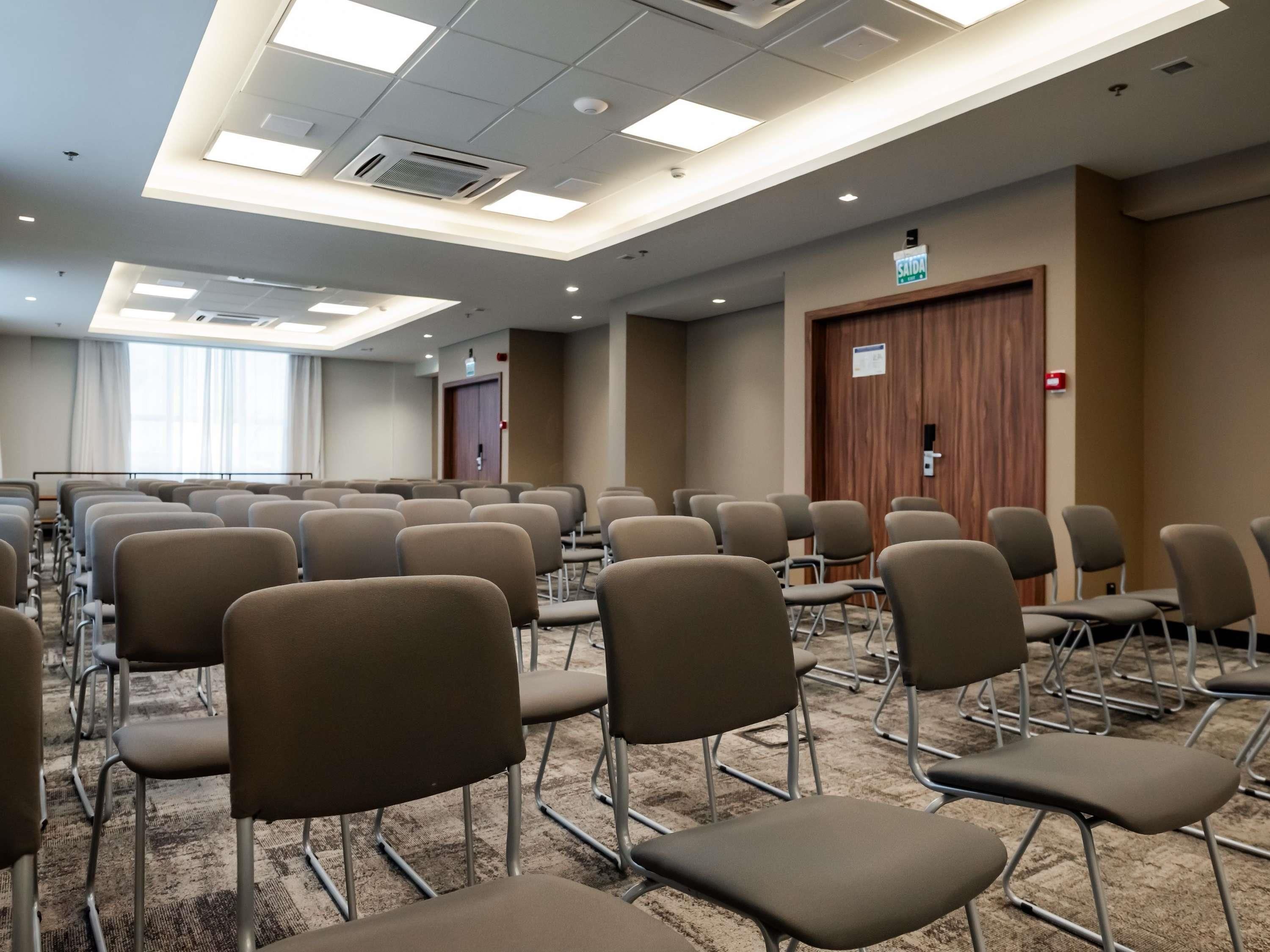 A conference room with rows of chairs, a carpeted floor, and a ceiling with recessed lighting.