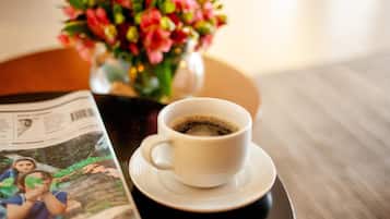 Una taza de café sobre un plato, una revista y un jarrón con flores sobre una mesa.