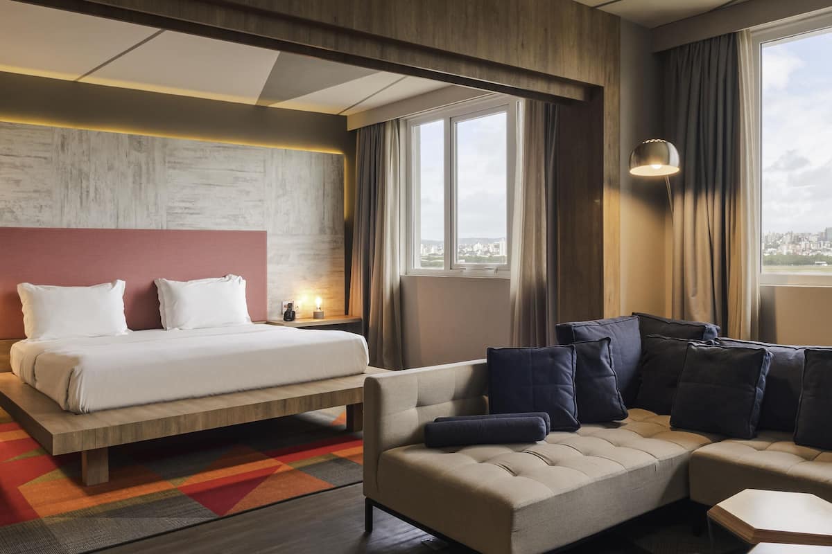 A modern hotel room with a large bed, a sofa, and a view of the city.