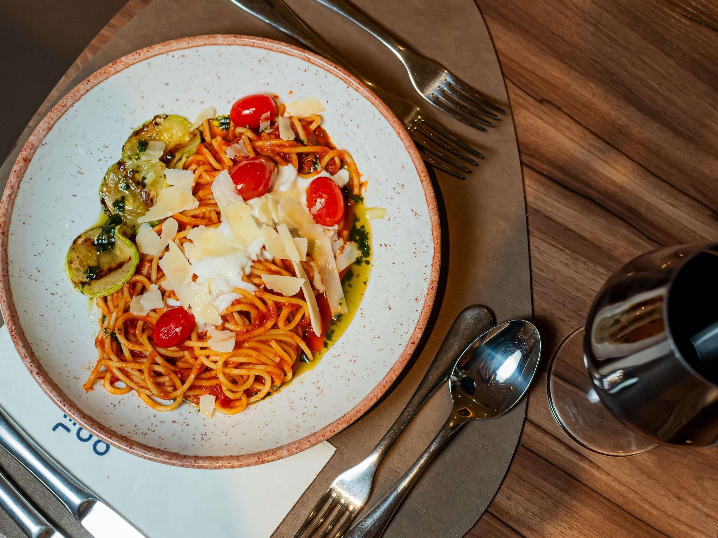 A plate of spaghetti with cherry tomatoes, cheese, and a green garnish on a speckled plate.