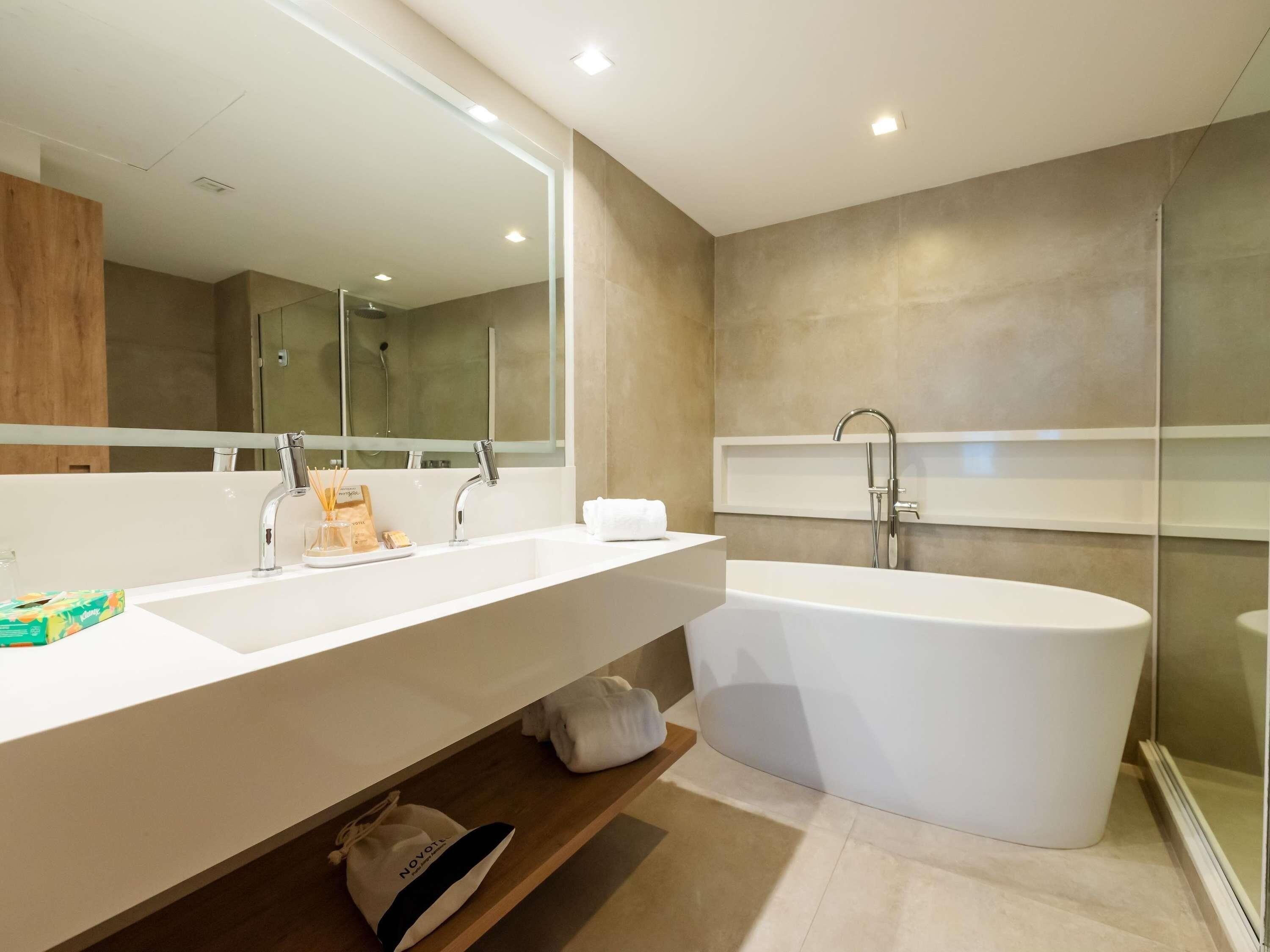 Un baño moderno con una bañera blanca grande, un lavamanos alargado con espejo y una zona de ducha.