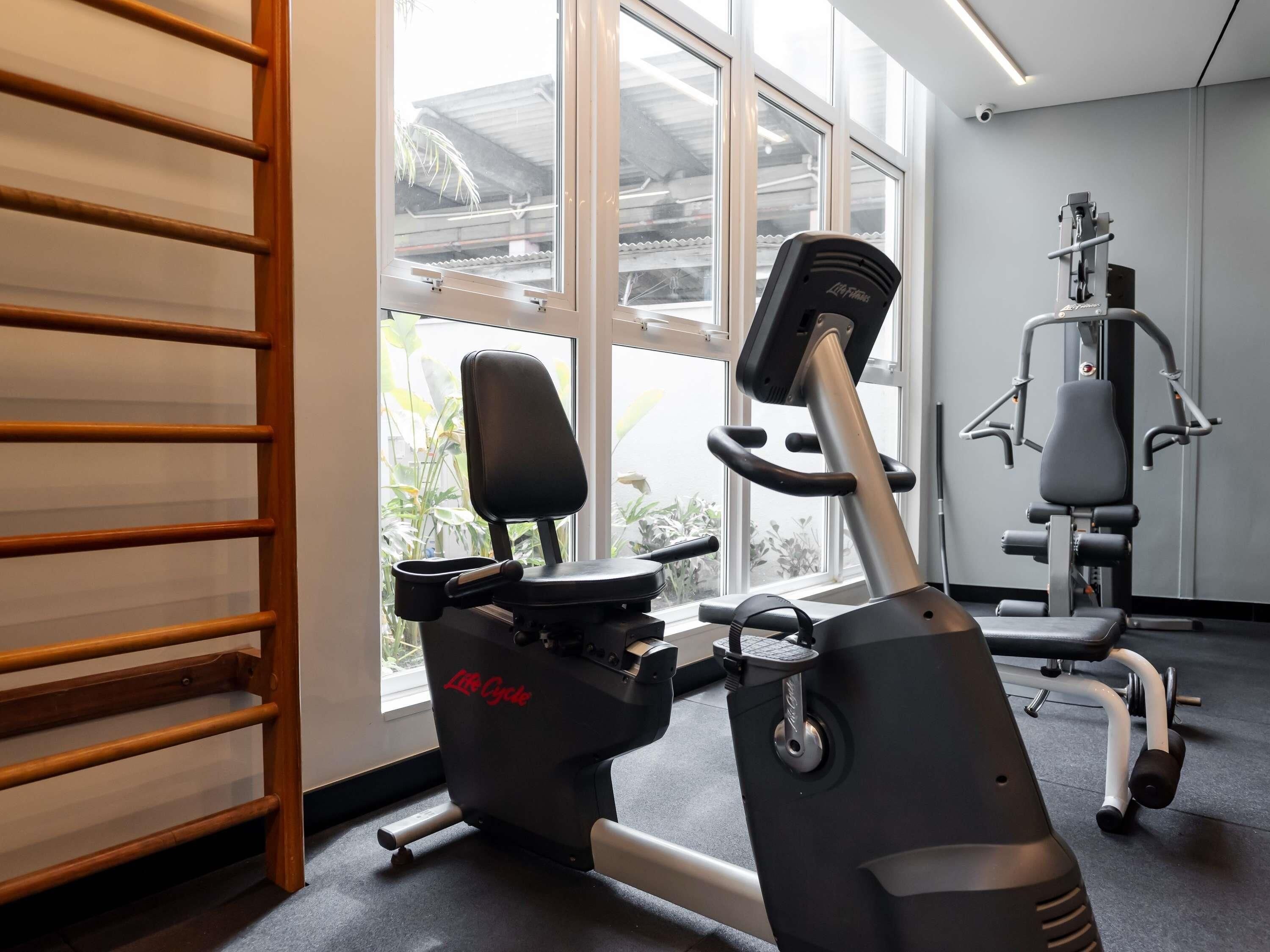 Une salle de sport équipée de matériel d’exercice, notamment un vélo elliptique et un vélo d’appartement, et une fenêtre donnant sur un paysage verdoyant.