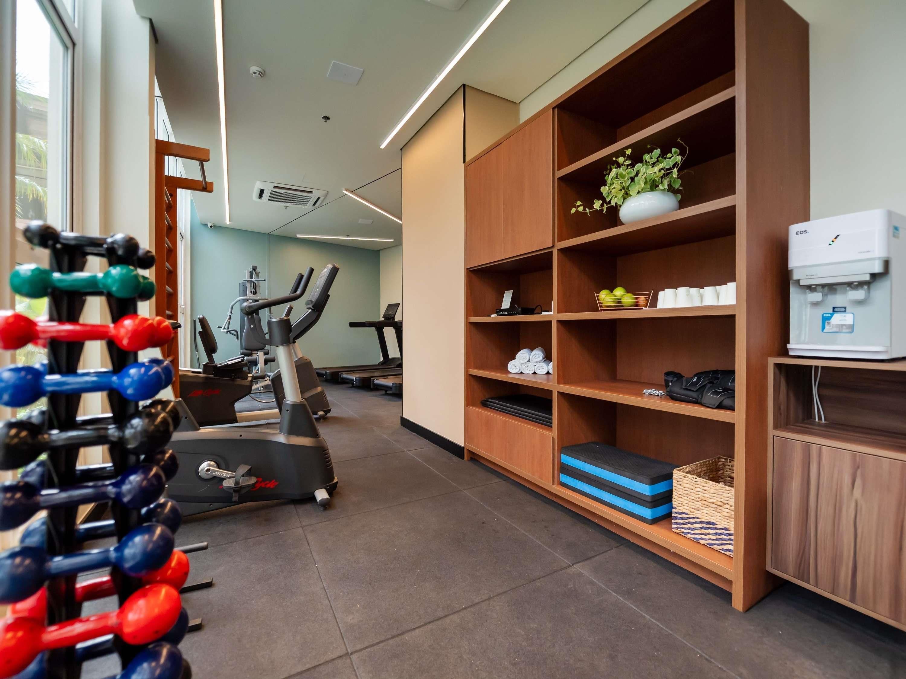 Un gimnasio con equipo de ejercicio, un dispensador de agua y estanterías.