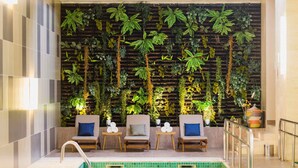 A pool area with a tiled floor, a pool with clear water, and a wall with various plants and a wooden slat design. - Novotel Porto Alegre Airport (Porto Alegre)