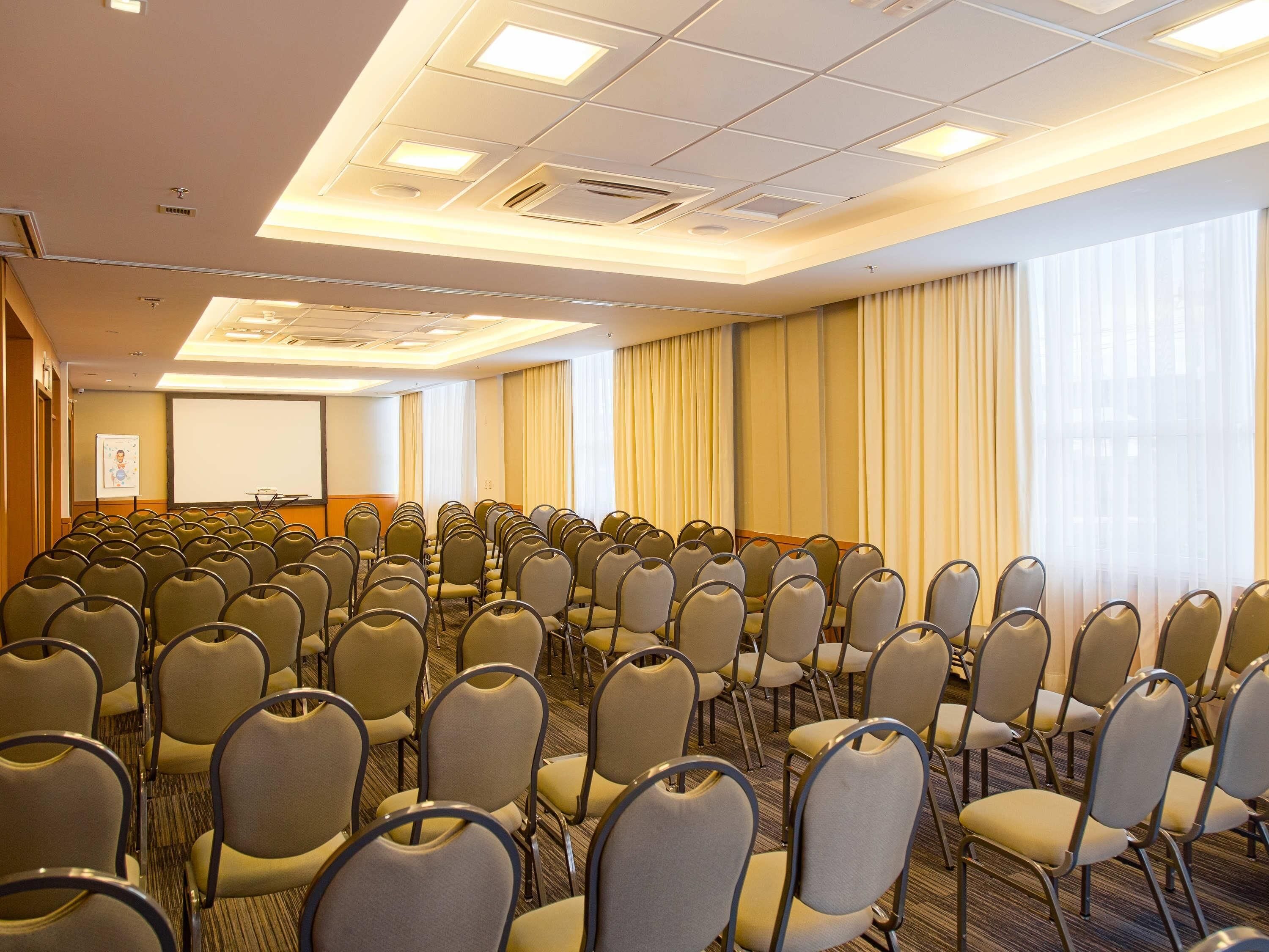 A conference room with rows of chairs, a projector screen, and a whiteboard.