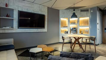 Una sala de estar moderna con un televisor de pantalla plana, un comedor con mesa y sillas de madera, y una cocina con iluminación empotrada.