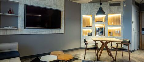 A modern living room with a flat-screen TV, a dining area with a wooden table and chairs, and a kitchen area with built-in lighting.