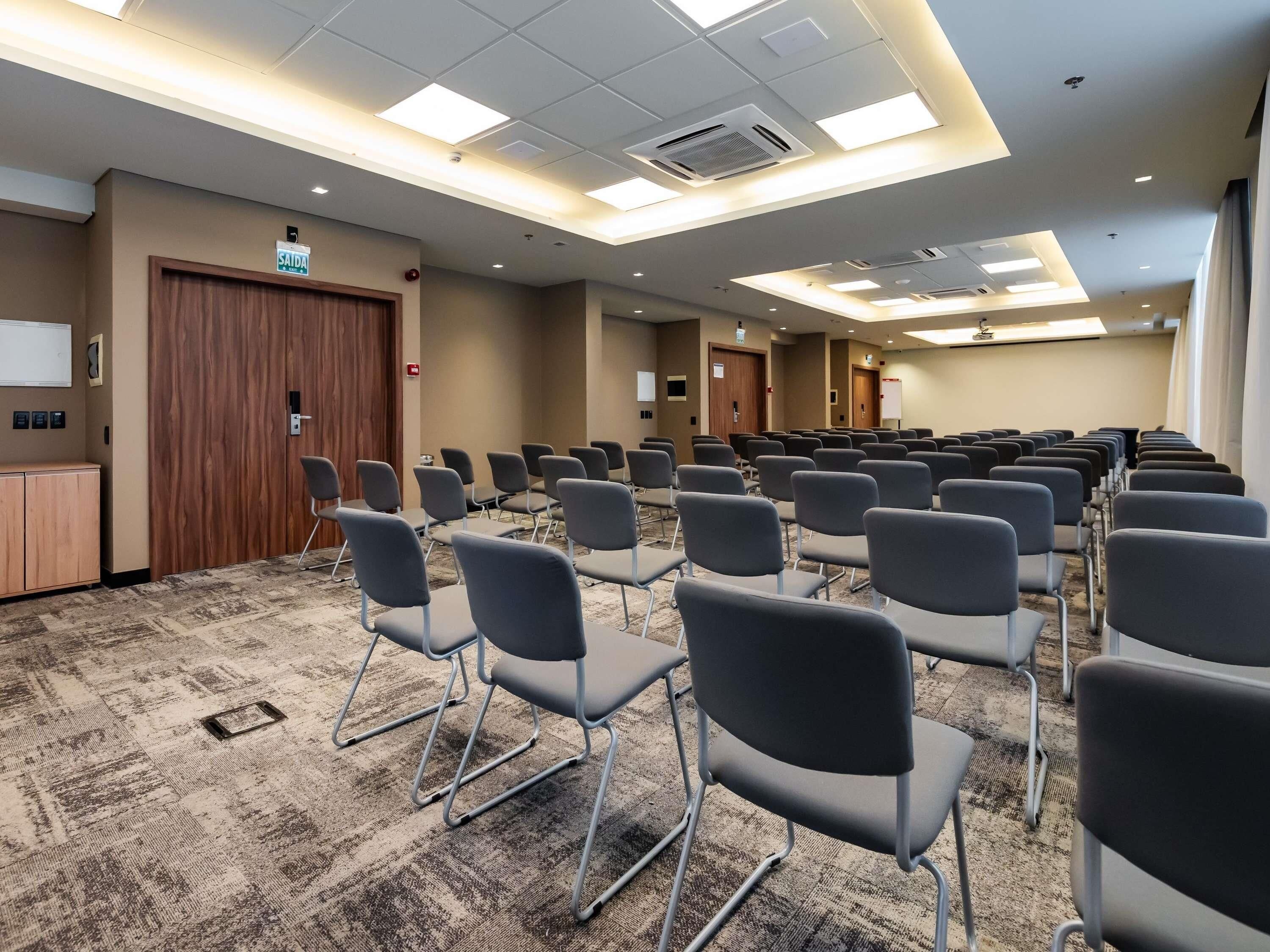 A conference room with rows of chairs, a carpeted floor, and a wooden door labeled 'SAIDA'.