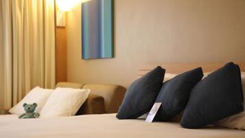 A hotel room with a bed, pillows, a teddy bear, and a painting on the wall.