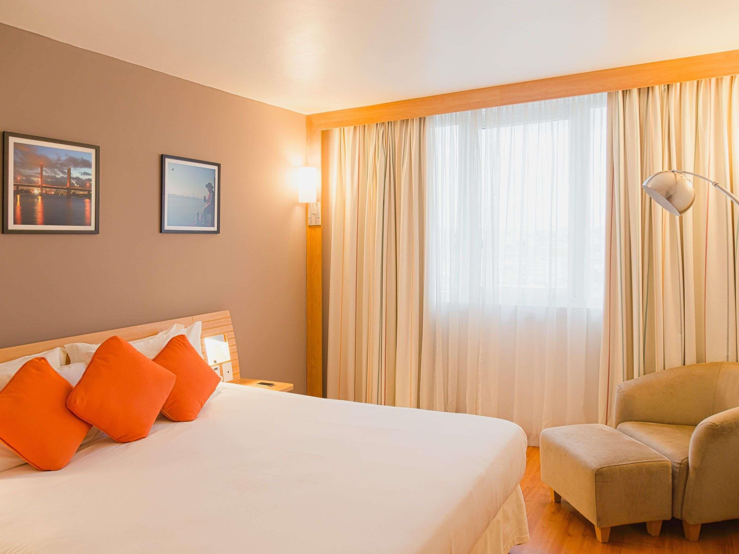 Una habitación de hotel con una cama, una silla y cortinas.