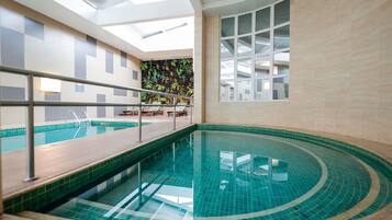 Una piscina interior con piso de vidrio, cubierta de madera y zona de estar con sillas y una mesa.